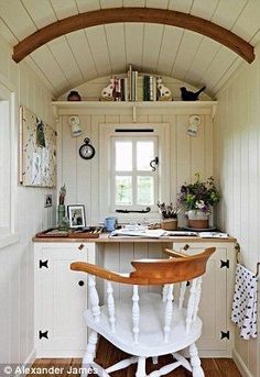 a kitchen with white walls and wooden flooring has an arched window above the sink