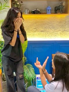 two women sitting down and one is covering her mouth while the other holds her hands up