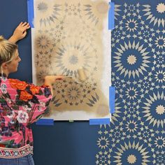 a woman is painting a wall with blue and white designs on it, while another woman holds a paintbrush in her hand