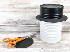 a white cup with scissors and a black top on a wooden table next to a pair of scissors