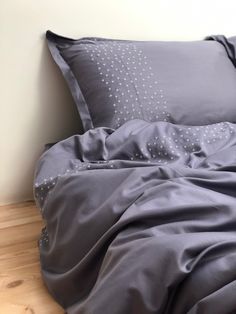 an unmade bed with grey sheets and pillows