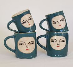 four mugs with faces painted on them are stacked in the shape of a woman's face