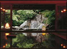 an indoor pool with waterfall and lanterns lit up at the end, surrounded by greenery