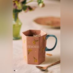 a pink coffee mug sitting on top of a table next to a fork and spoon