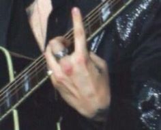 a close up of a person holding a guitar and making the peace sign with their fingers