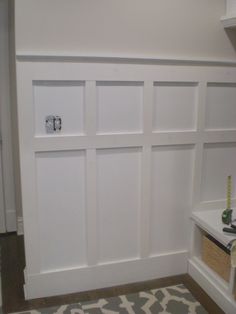 a room with white paneling and shelves on the wall