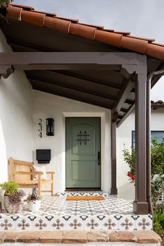 a green door sits on the side of a white house with tiled steps and potted plants