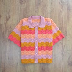 a pink, yellow and orange knitted cardigan sitting on top of a wooden floor