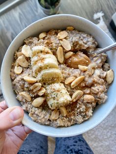 a person holding a bowl of oatmeal with banana slices and almonds