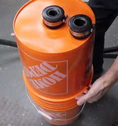 a man is holding an orange propane tank with two black caps on it's top