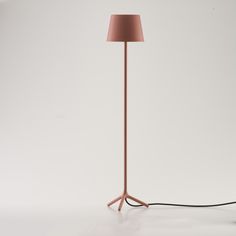 a floor lamp with a pink shade on the base and a black cord connected to it