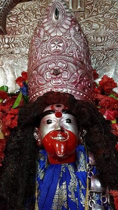 an elaborately decorated mask is displayed in front of red flowers