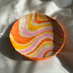 an orange and pink bowl sitting on top of a white sheet