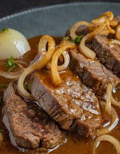 a close up of food on a plate with onions and meat in gravy