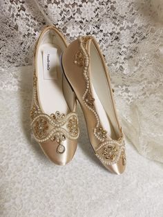 two pairs of gold shoes with beading on the bottom and side, sitting on a lace covered surface