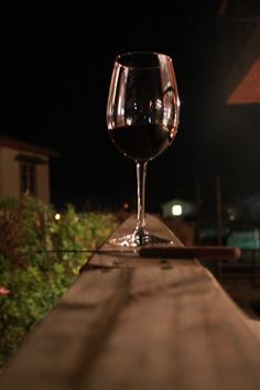 a glass of wine sitting on top of a wooden table next to a building at night