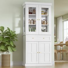 a tall white cabinet sitting next to a potted plant on top of a hard wood floor