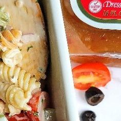 a pasta salad in a white dish next to a bag of dressing and a bottle of dressing