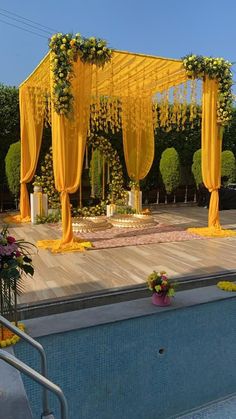 an outdoor wedding setup with yellow draping and flowers on the ground next to a swimming pool