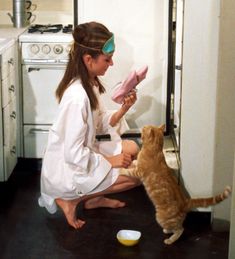 a woman sitting on the floor with a cat looking at something in front of her