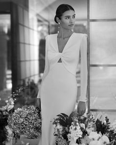 a woman in a white dress standing next to flowers