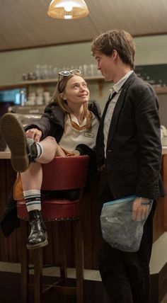 a man and woman standing next to each other in front of a bar with stools