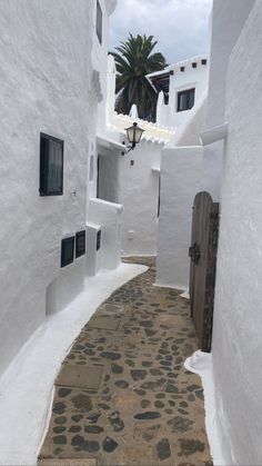 an alley way with white walls and cobblestone pavement leading to a door in the center