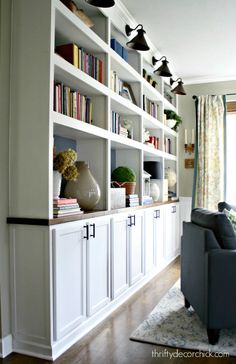 a living room filled with lots of white bookshelves next to a gray couch