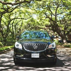 a black car parked on the side of a road next to lots of trees and grass