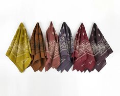 five different colored bandanas hanging on a white wall with one folded and the other unzipped