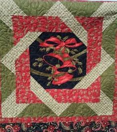 a quilted wall hanging with red and green flowers on it's center piece