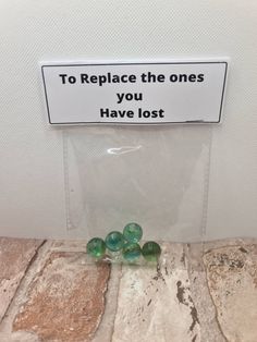 some green marbles sitting on top of a tile floor next to a sign that says, to replace the ones you have lost