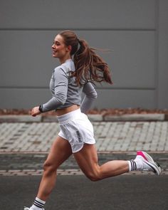 a woman is running on the street with her hair blowing in the wind and wearing white shorts