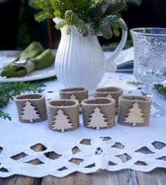 a table topped with cups and plates covered in burlap next to a vase filled with greenery