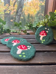 two green felt coasters with red mushrooms on them sitting next to a potted plant