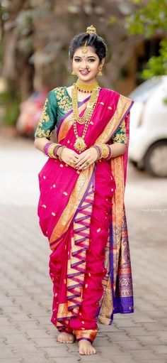 a woman in a pink and green sari with gold jewelry on her neck, standing outside