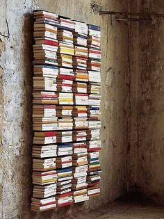 a large stack of books sitting on top of a cement floor next to a wall