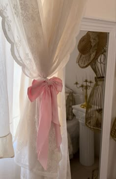 a pink bow tied to the back of a white curtain in a room with lace curtains