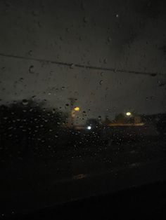 rain is falling on the windshield of a car at night with street lights in the background