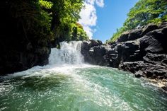 the water is green and flowing down the side of a waterfall with trees in the background