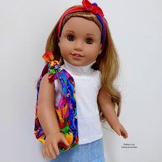 a doll wearing a white shirt and blue skirt with a red bow on her head