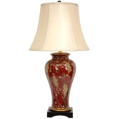 a red and gold vase lamp with a white shade on the top, sitting on a black base