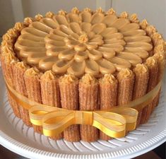 a cake on a plate with a yellow ribbon around it and frosting in the shape of a flower