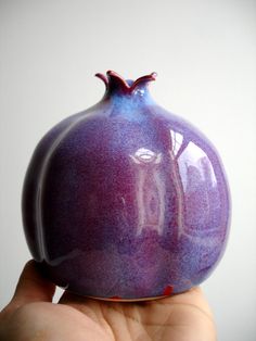 a hand holding a small purple vase in it's palm, against a white background