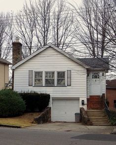 a white house sitting next to a street with trees on both sides and stairs leading up to the front door