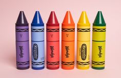 four crayons are lined up in a row on a pink background, one is yellow and the other is blue