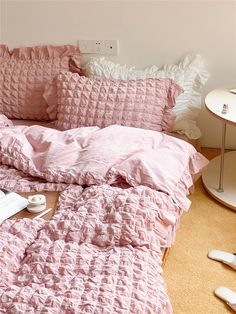 a bed with pink comforter and pillows on it next to a lamp, phone and other items