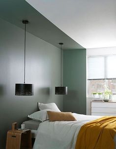 a bed sitting in a bedroom next to a window with two lamps hanging above it