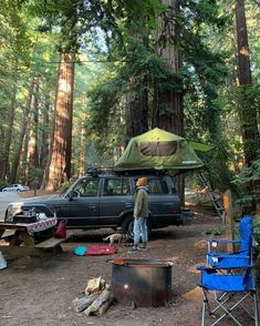 a man standing in front of a tent next to a parked car and campfire