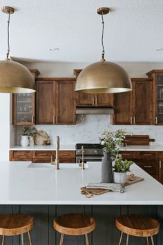 three lights hanging over a kitchen island with wooden stools and white counter tops in front of it